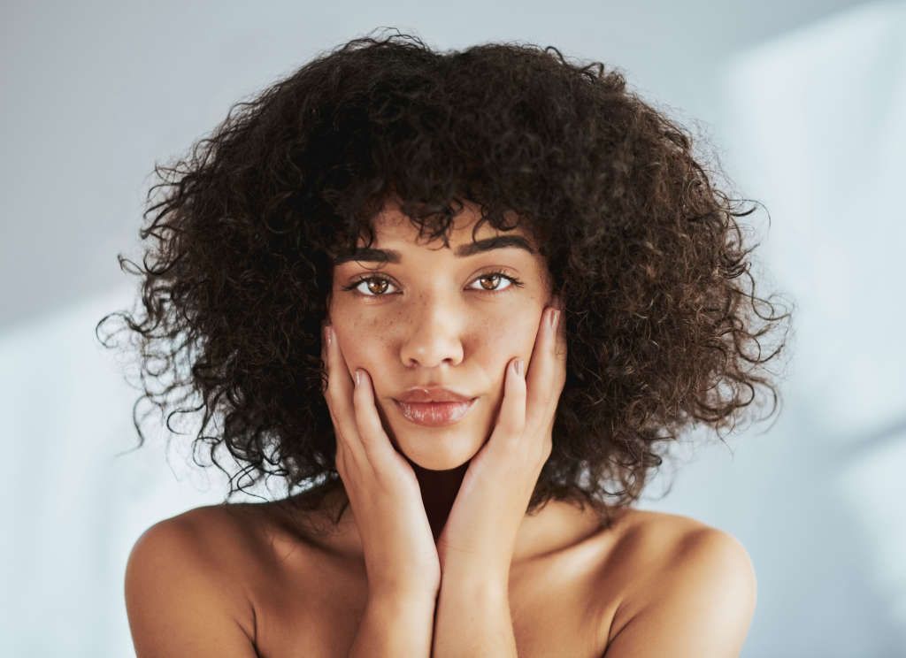 Woman with curly hair, hands on face.