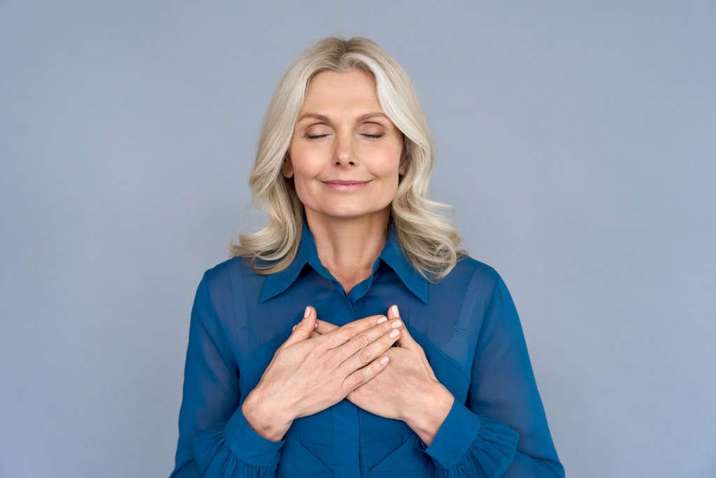 Woman smiling with hands on heart, serene expression.