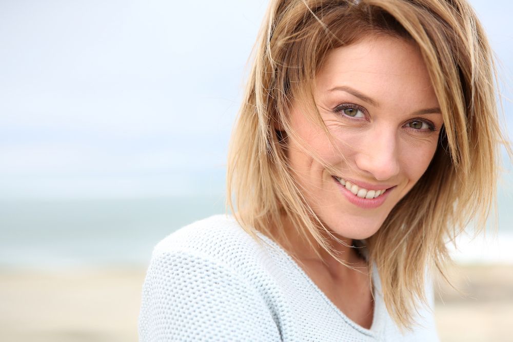 Smiling woman with wind-blown hair outdoors.