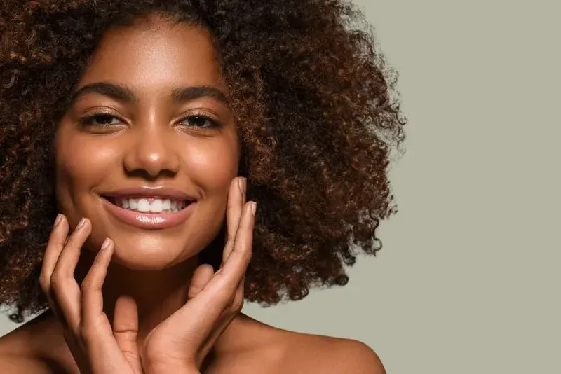 Smiling woman with curly hair on neutral background.