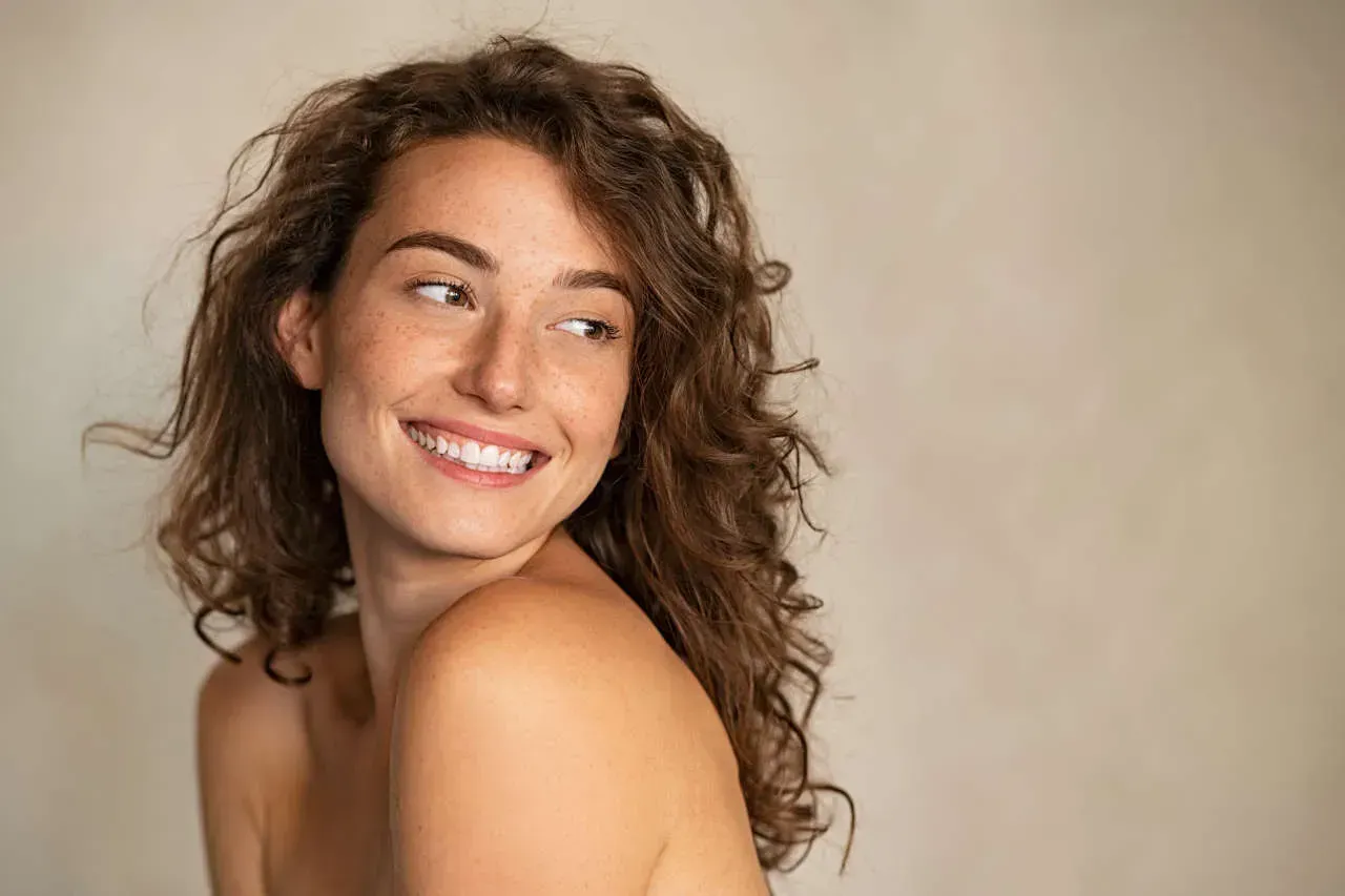 Smiling woman with curly hair against neutral background.