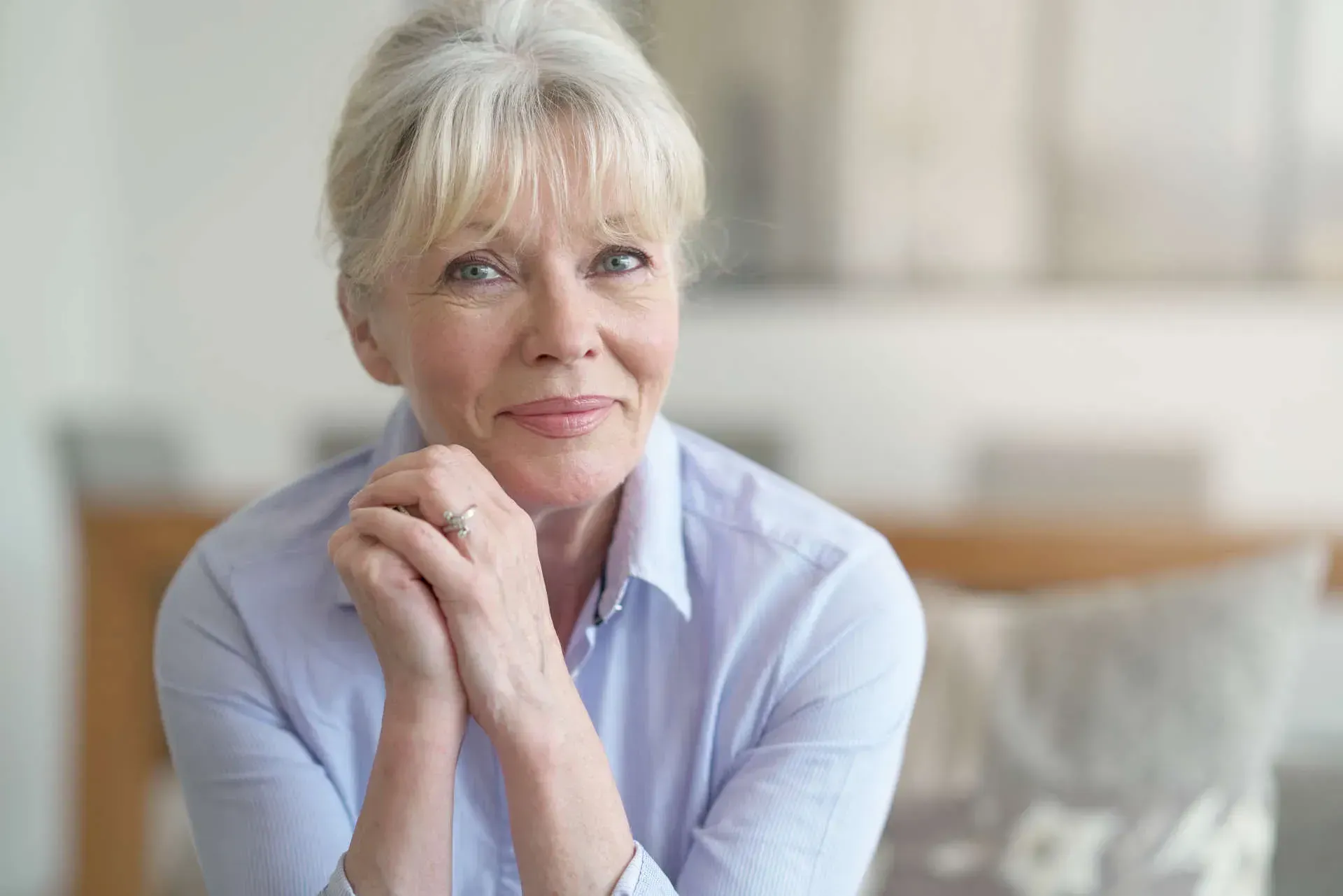 Smiling older woman with hands clasped thoughtfully.