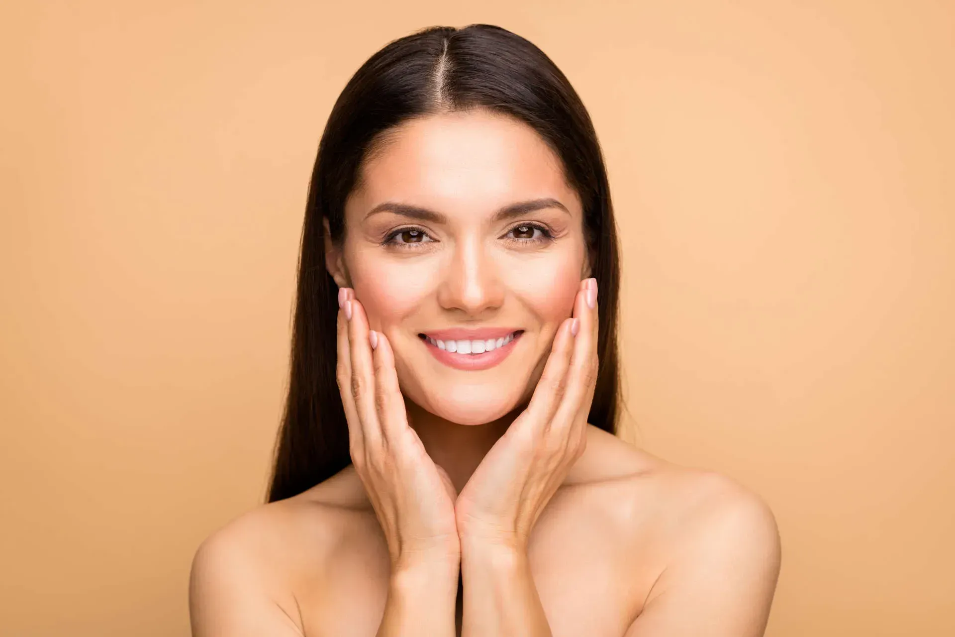 Smiling woman touching her face, neutral background.