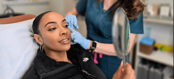 Smiling woman applying skin care in mirror.