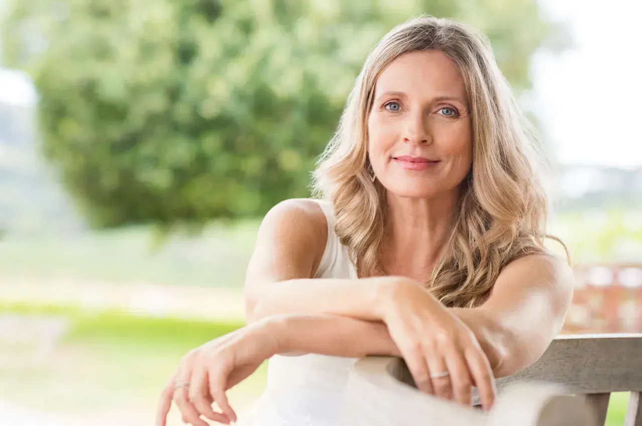 Smiling woman sitting outdoors with hands resting.