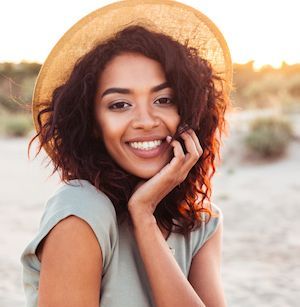 Smiling woman in straw hat at sunset beach.