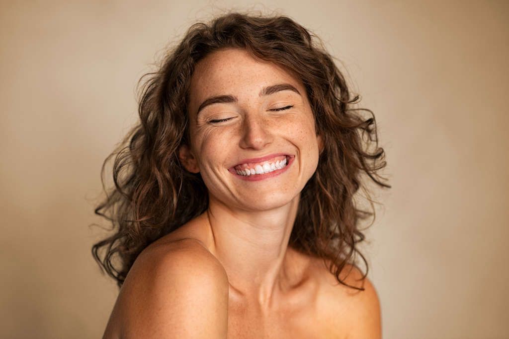 Smiling woman with curly hair against soft background.