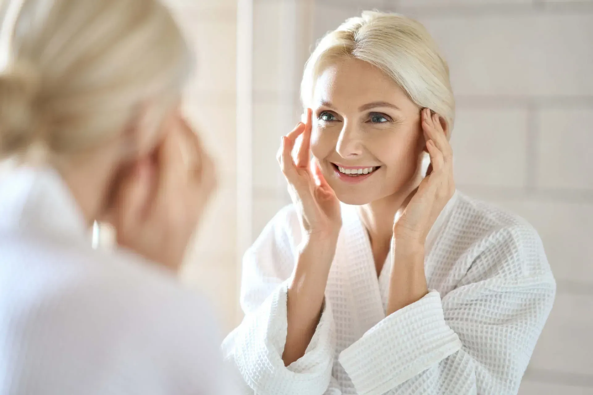 Woman smiling in bathrobe, applying skincare.