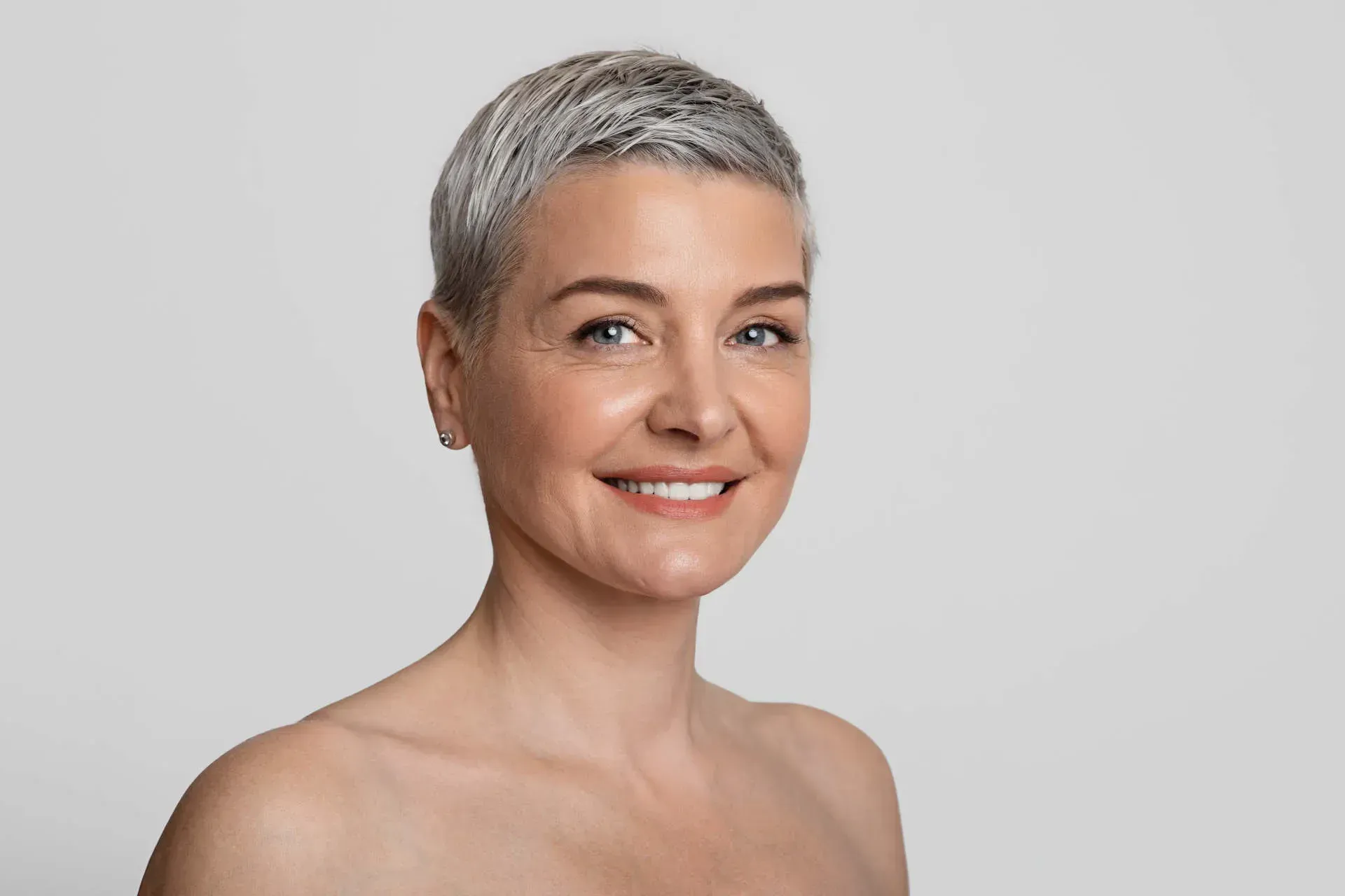 Smiling woman with short gray hair and earrings.